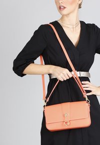 Borsa a tracolla in pelle pesca con finitura testurizzata, hardware dorato e tracolla regolabile; presenta un flap anteriore e chiusura a gancio.