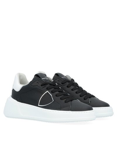 Black leather sneakers with white rubber sole, textured accents and stitched detailing. Features black laces and a grey logo patch on the side.
