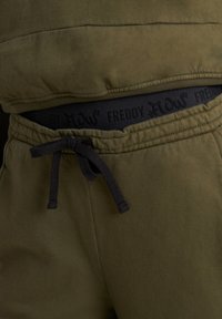 Pantalones joggers color verde oliva con cintura elástica negra con la marca "FREDDY", cordón ajustable y textura suave. Diseño informal.
