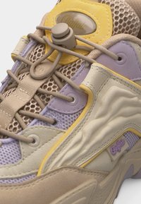 Baskets chunky avec panneaux en mesh et cuir beige, jaune et lavande, lacets élastiques à réglage par cordon, et détails en forme de vague embossés sur le côté.