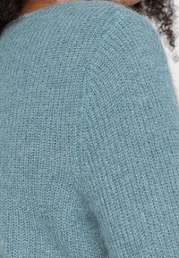 Strickpullover aus weichem, strukturiertem, hellblauem Stoff mit lockerer Passform. Die Oberfläche zeigt ein deutlich sichtbares offenes Maschenmuster.