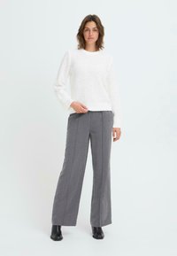 White textured knit sweater with long sleeves, paired with high-waisted gray wide-leg trousers and black ankle boots. Simple, structured design.