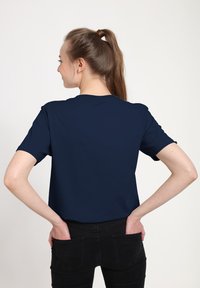 T-shirt a maniche corte blu navy in tessuto morbido, con collo tondo e vestibilità rilassata. Indossato con jeans neri, mani infilate nelle tasche.