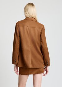 Blazer en daim marron avec une coupe classique, une fente arrière simple et des poignets boutonnés. Texture douce avec une finition lisse. Design minimaliste.