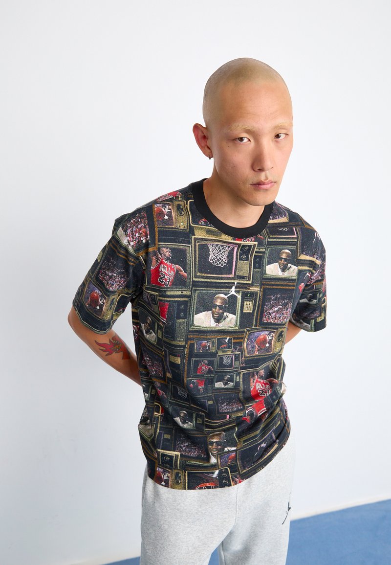 T-shirt noir à manches courtes présentant un collage d'images sur le thème du basketball à l'intérieur d'écrans de télévision. Comprend des couleurs vives et des graphismes détaillés.