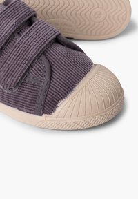 Purple corduroy sneakers with beige rubber soles, featuring dual velcro straps and a textured, protective toe cap. Textured tread pattern.