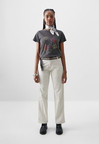 Grafisk svart t-shirt med röd och guld design; krämfärgade vida byxor; svarta stövlar; silveraccessoarer; vit mönstrad scarf.