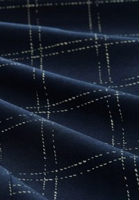 Námořnická látka se vzorem mřížky vytvořeným bílým stehem. Textura vypadá hladce s jemnými sklady, což naznačuje, že je dobře poddajná.