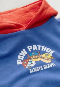 Blaues Kapuzenpullover mit roter Kapuze. Der Frontdruck zeigt drei Cartoonfiguren mit dem Text "PAW PATROL IMMER BEREIT!" Weicher Baumwollstoff.