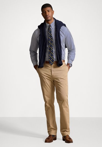Marinblå kabelstickad tröja över en blårandig skjorta med ett mönstrat slips, i kombination med beige chinos och bruna läder loafers.