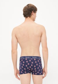 Marineblaue Boxershorts mit einem sich wiederholenden Muster aus roten und weißen Fahrzeugen. Der elastische Bund zeigt den Markennamen in weißer Schrift. Weicher Stoff.