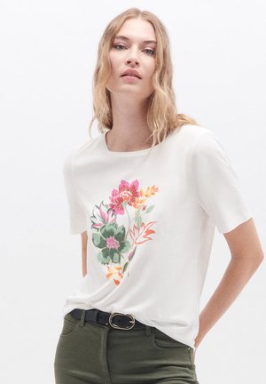 T-shirt bianco a maniche corte con un design floreale colorato in rosa, verde e giallo. Il tessuto appare morbido e ha un colletto rotondo.