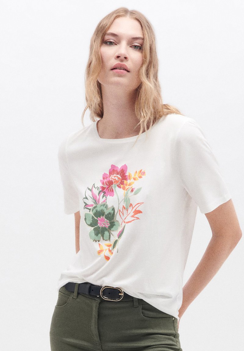 Camiseta blanca de manga corta con un diseño floral colorido en rosa, verde y amarillo. La tela parece suave y tiene un cuello redondo.