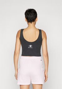 Must have mustakirju mustriga crop tank top ümarate seljaga, millel on valge "Champion" logo. Koos helekarmi värvi lühikesed püksid, küljetaskutega.