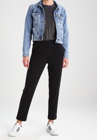 Denim jacket, light blue, fitted design with button closures. Dark black tapered pants, smooth texture, paired with white sneakers featuring black stripes.