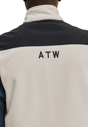 Fleecetröja med hög krage, i krämfärgad kropp och svarta samt mörkblå accenter. Broderad "ATW" logotyp på baksidan.
