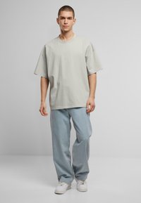 Hellgrünes, übergroßes T-Shirt mit kurzen Ärmeln, kombiniert mit lockeren, hellblauen Jeans und weißen Sneakers. Einfaches Design, aus Baumwollmaterial.