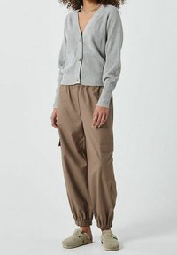 Grå ribbad cardigan med v-ringning och guldfärgad knappar, matchad med bruna cargobyxor med elastiska muddar och sidofickor, bärs tillsammans med gråtofflor.