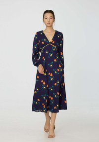 Robe florale bleu marine avec des manches longues, décolleté en V et bord jaune ; présente des motifs de fleurs orange et turquoise et une silhouette fluide.