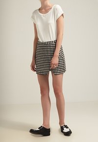 T-shirt bianco a maniche corte abbinato a pantaloni corti a scacchi in bianco e nero. Scarpe in bianco e nero con dettagli della cinturina. Tessuto a trama liscia.