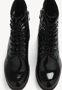 Bottes de cheville en cuir verni noir avec un bout rond, dotées de lacets à l'avant et de fermeture éclair sur les côtés pour un accès facile. Fini brillant texturé.