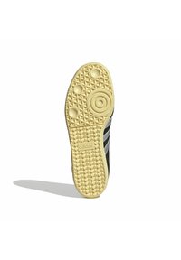 Černá podrážka tenisky se žlutou gumou, s texturovaným vzorem ve tvaru diamantů a třemi kruhovými akcenty. Viditelné logo "adidas".