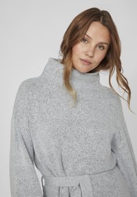 Pull à col roulé en tricot gris avec des manches longues, une taille ceinturée et une texture douce. Présente une coupe confortable et décontractée ainsi qu'un motif subtil.