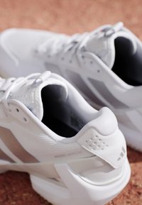 Een paar witte sportschoenen met beige strepen en gevoerde zolen geplaatst op een roodbruine ondergrond.