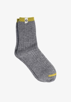 Par de calcetines grises acanalados de longitud media con puños amarillos y pequeño detalle amarillo en la punta, mostrados sobre un fondo blanco.