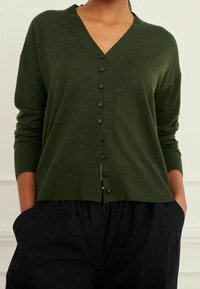 Cardigan verde oliva realizzato in morbido tessuto a maglia, con scollo a V, chiusura frontale a bottoni e polsini e orlo a coste.