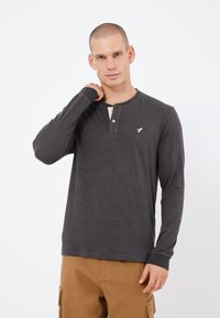 Dark gray long-sleeve shirt with a henley neckline, two buttons, and a light-colored placket. Features a small logo on the chest.