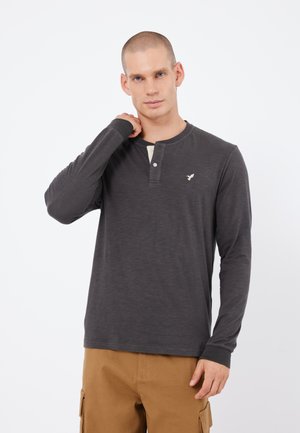 Dark gray long-sleeve shirt with a henley neckline, two buttons, and a light-colored placket. Features a small logo on the chest.