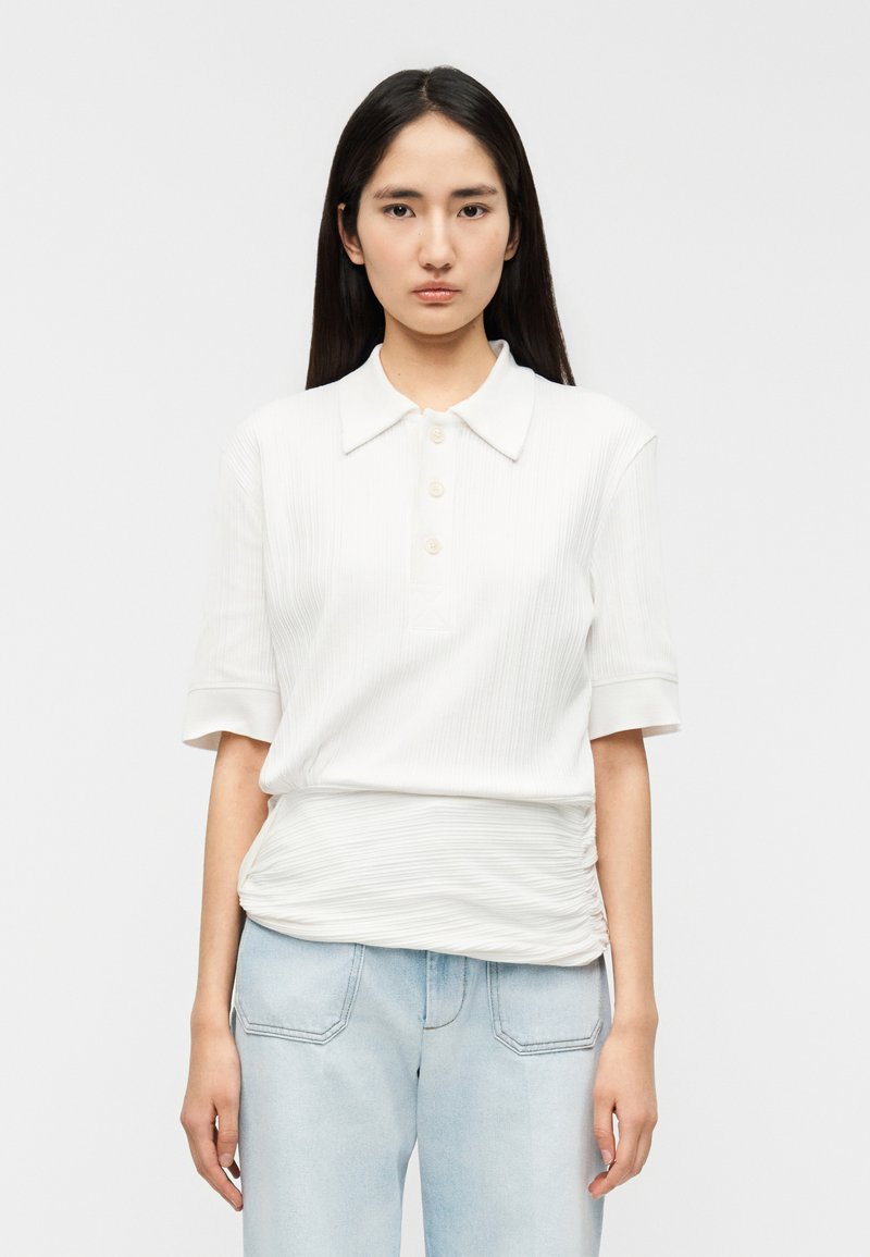 Polo blanc avec un motif texturé côtelé, manches courtes, trois boutons, coupe décontractée, associé à un jean en denim bleu clair.