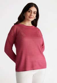 Pullover a maniche lunghe, con texture, di un intenso colore rosa con righe orizzontali. Materiale morbido, vestibilità rilassata, abbinato a pantaloni bianchi.