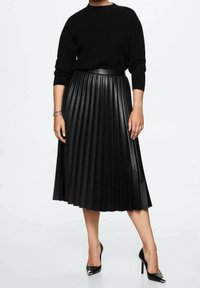 Jupe plissée noire en matériau synthétique, avec une taille haute et une texture brillante, associée à un pull en maille noir et des escarpins.
