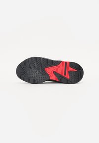 Semelle de chaussure avec une base en caoutchouc noir et un accent rouge, présentant un motif de grip texturé et un dessin de bande de roulement prononcé pour une meilleure traction.