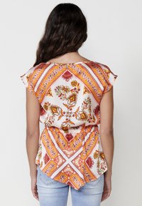 Top de manga corta con un patrón floral y paisley, presentando detalles en naranja y rojo sobre un fondo blanco, con escote en la espalda y cintura fruncida.