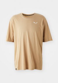 T-shirt in cotone beige con collo rotondo, maniche corte e logo bianco sul lato sinistro del petto. Tessuto morbido, vestibilità classica, senza motivi visibili.