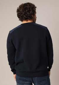Pull marine sombre en tissu texturé, avec des panneaux d'épaule bleus contrastants, col rond et poignets et ourlet côtelés.