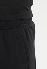 Shorts de sport noirs avec une taille élastique, des poches et une texture de tissu lisse et douce. Le design est simple et fonctionnel.