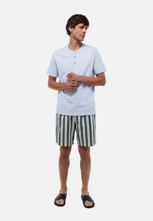 Chemise à manches courtes bleu clair avec trois boutons dorés, associée à un short rayé vert, bleu et crème, portée avec des sandales noires.