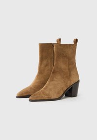 Bottes ankle en suède tan avec des bouts pointus et de petits talons carrés, dotées d'une fermeture éclair latérale et de petites poignées en haut.