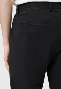 Svarta byxor med en slät yta, med en enda bakficka och en slim-fit design. Midjebandet är diskret och utan prydnader.