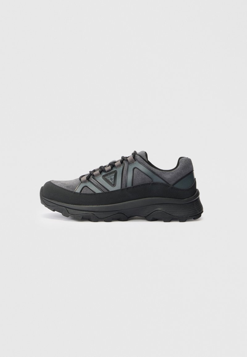 Grey and black low-top sneaker with thick sole, lace-up front, and triangular logo on side against white background.
