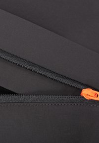 Sort stof med to lynlåse; den ene har et orange træk. Glat tekstur, med et rent, minimalistisk design og kontrasterende syninger.