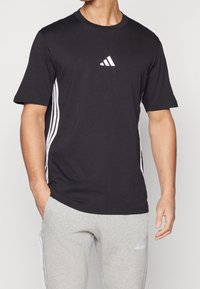 Svart atletisk t-shirt med rund halsringning, korta ärmar och vita tre-randiga detaljer på sidorna; har en liten vit logotyp på bröstet.