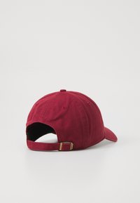 Maroon cotton baseball cap with a curved brim, adjustable strap, metal hardware, and visible stitching. Smooth texture with no patterns.