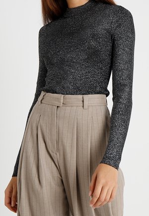 Un haut noir à paillettes à manches longues avec un col haut, associé à un pantalon beige à rayures fines taille haute avec des détails plissés.