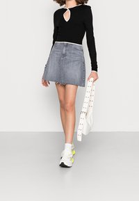 Svart långärmad topp med ett nyckelhål i halslinningen, kombinerad med en denimkjol med fransar. Vit handväska med nitar på remmen och färgglada sneakers.