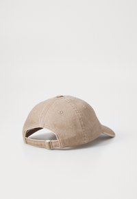 Baseball cap in light brown fabric with a soft texture, adjustable strap at the back, and six-panel design with stitching details.
